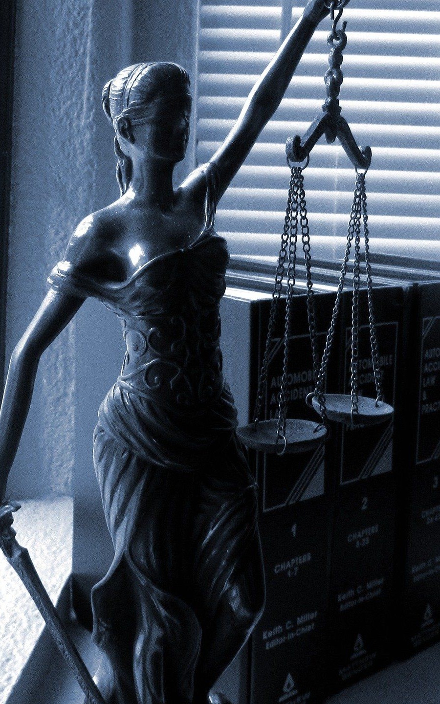 Statua della Giustizia con la bilancia, davanti a volumi di diritto