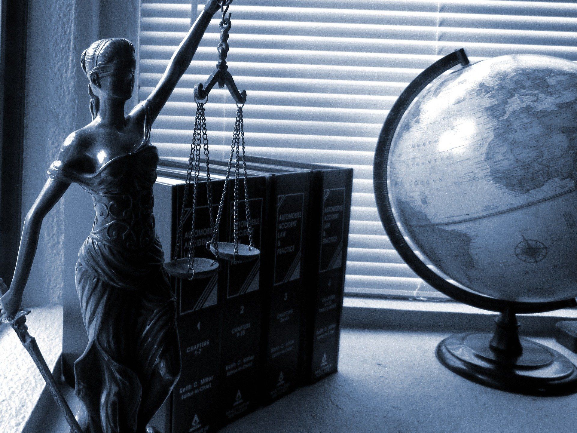 Una statua della Giustizia accanto a volumi di diritto e a un mappamondo